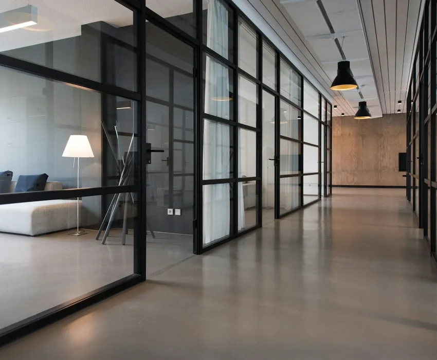 A bright office corridor with glass partitions and a comfortable seating area