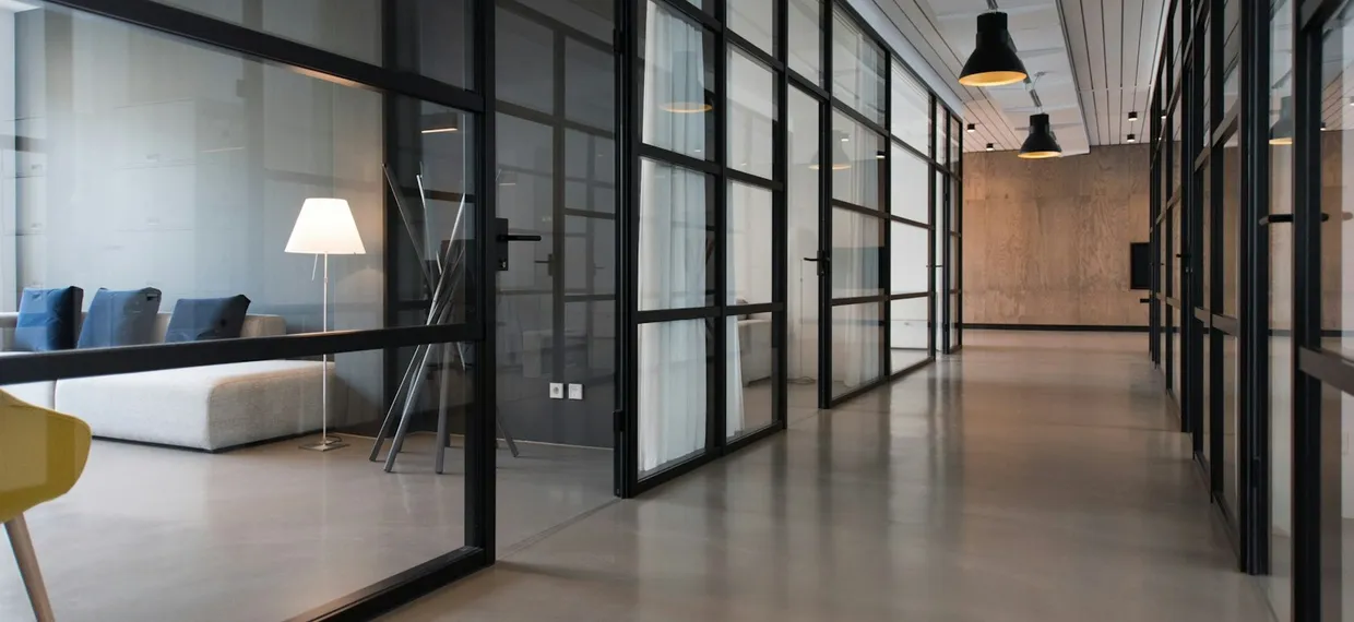 A bright office corridor with glass partitions and a comfortable seating area