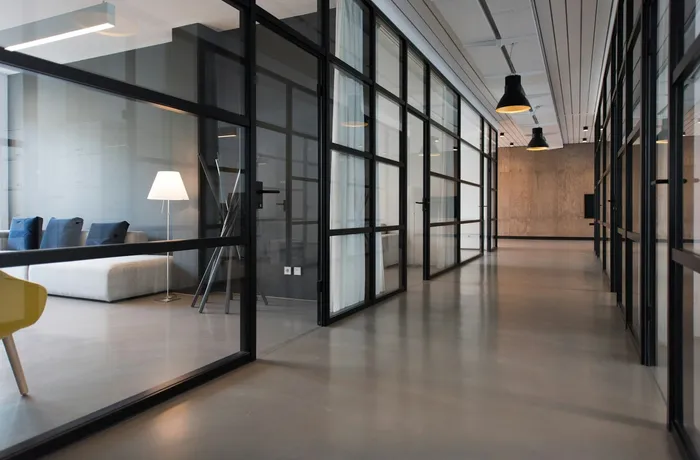 A bright office corridor with glass partitions and a comfortable seating area